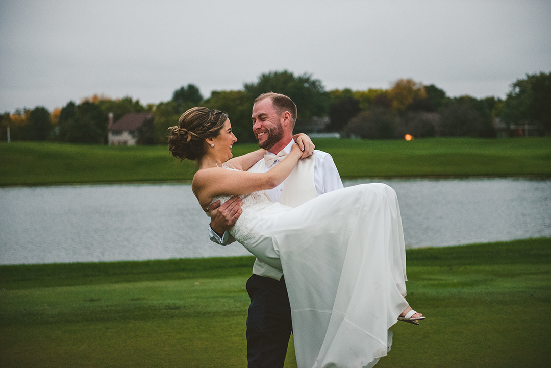 a groom carrying his bride at the Cress Creek Country Club in Naperville as they look at each other and laugh