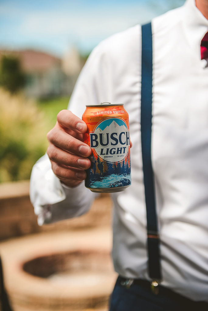 a groomsmen holding a orange busch light can as he stands around talking to his friends