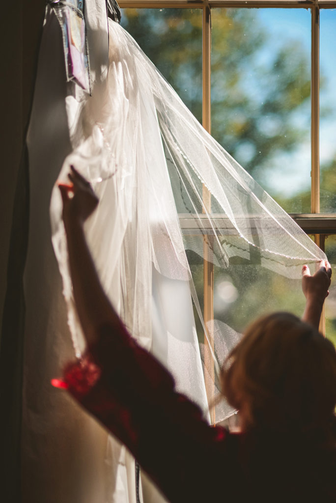 a bridesmaid adjusting the brides veil in front of a window