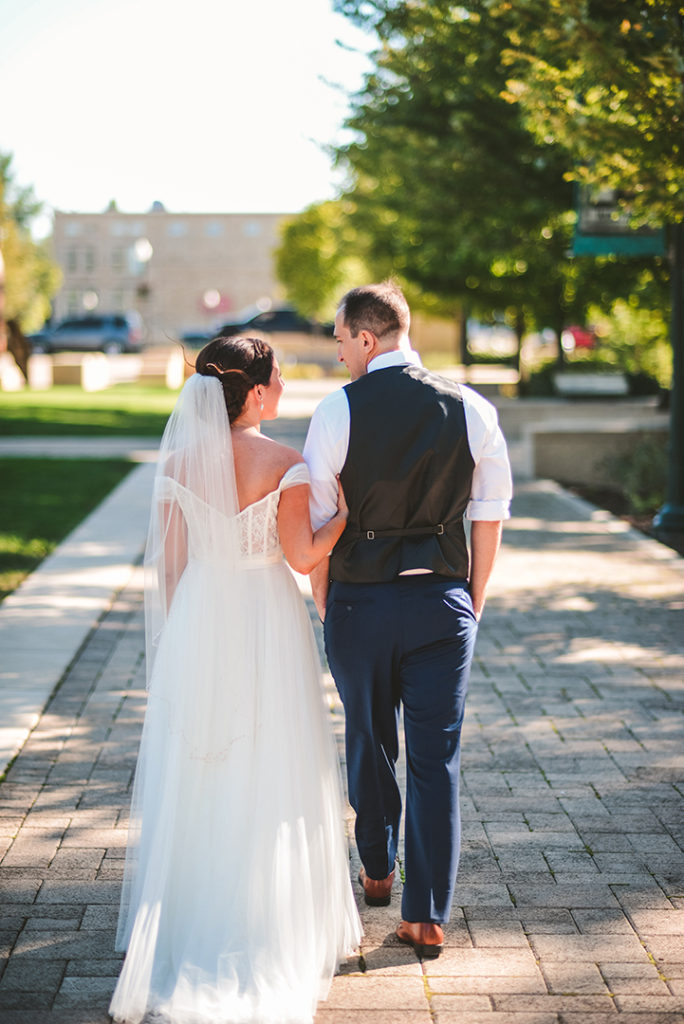 a bride holding onto her grooms arm as they walk down a path in Lockport