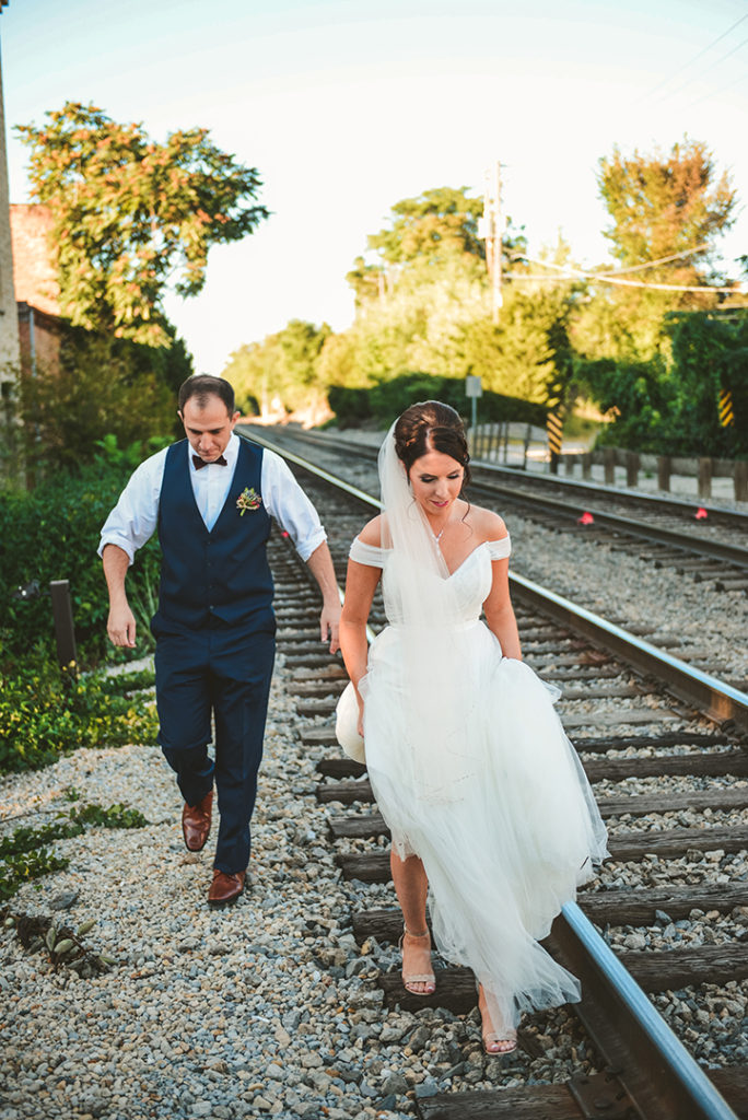 the bride and groom walking down train tracks as the bride holds up her dress