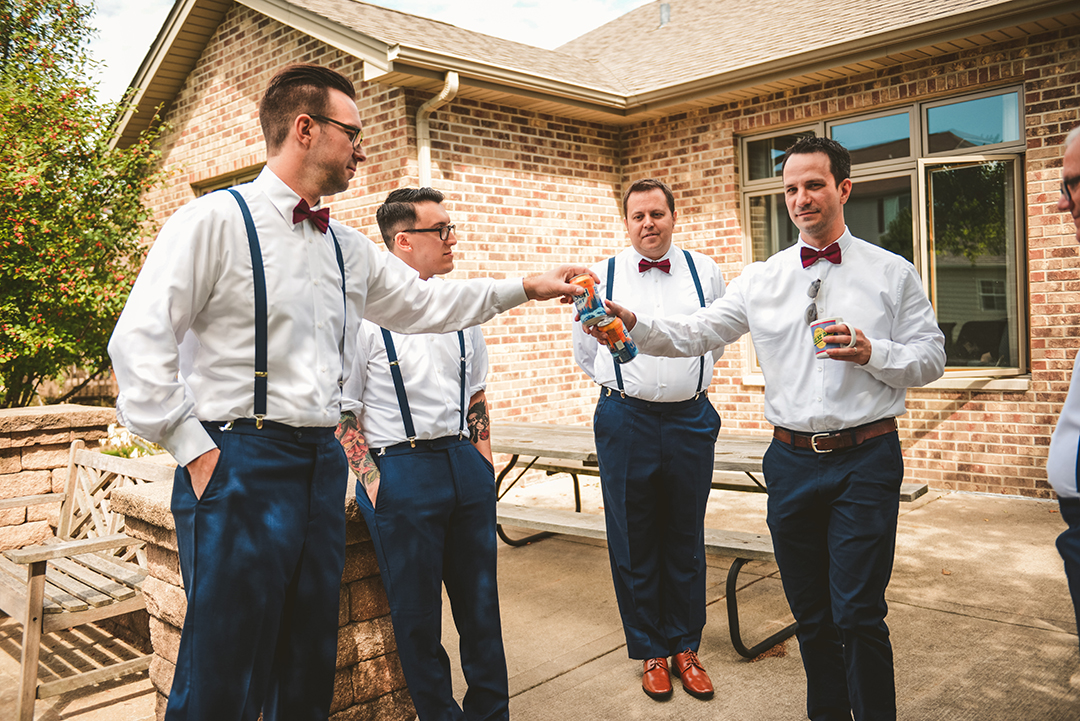 the groomsmen handing each other beer at a wedding as the groom gets ready