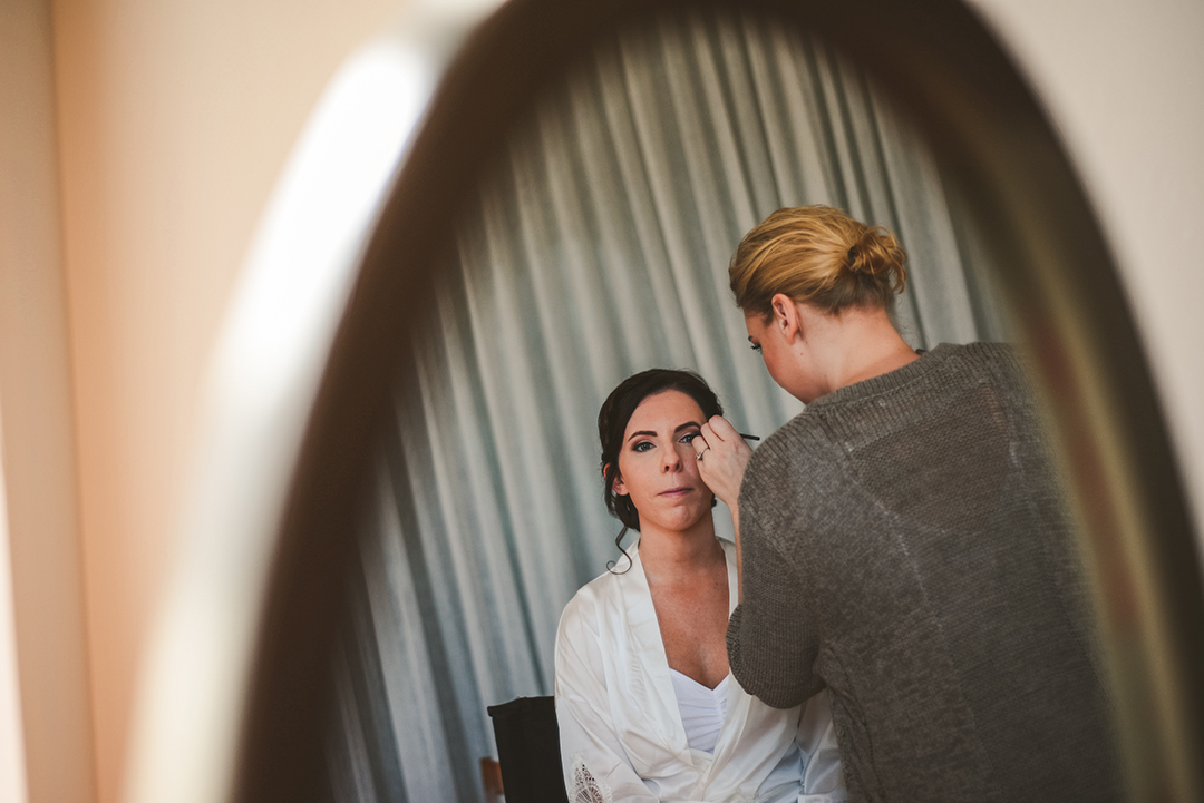a reflection in a mirror of a makeup artist applying makeup to the bride at historic building in Lockport IL