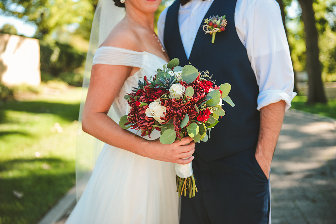 a detail photo of a bride holding her bouquet as her groom has his hand in his pocket