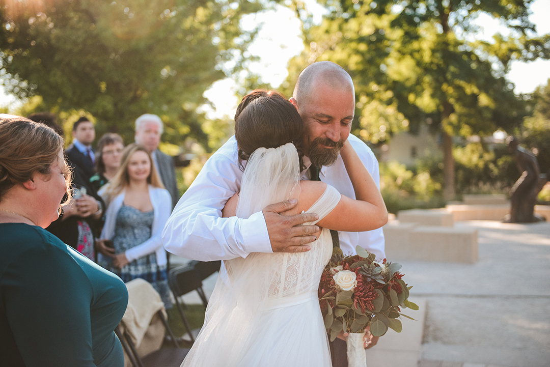 the father of the bride hugging his daughter as she is about to get married outside in a park in Lockport