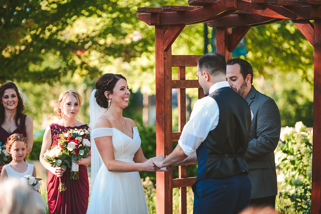 the bride laughing during her wedding ceremony as her groom holds her hands outside at a park in Lockport