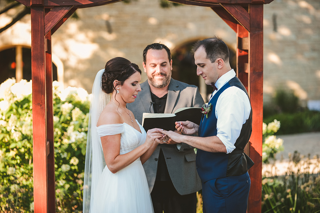 the bride placing a ring on her grooms finger during their wedding ceremony