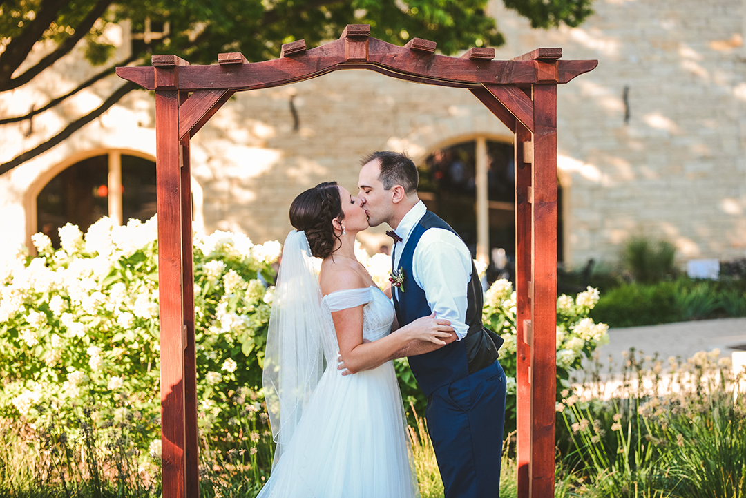 the bride and groom kissing for the first time under an arch in a park in Lockport IL