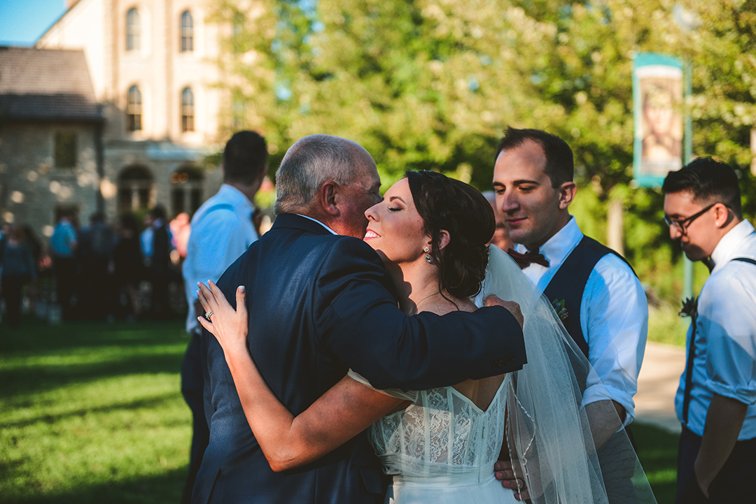 the father of the bride hugging his daughter after she just got married as her groom looks on