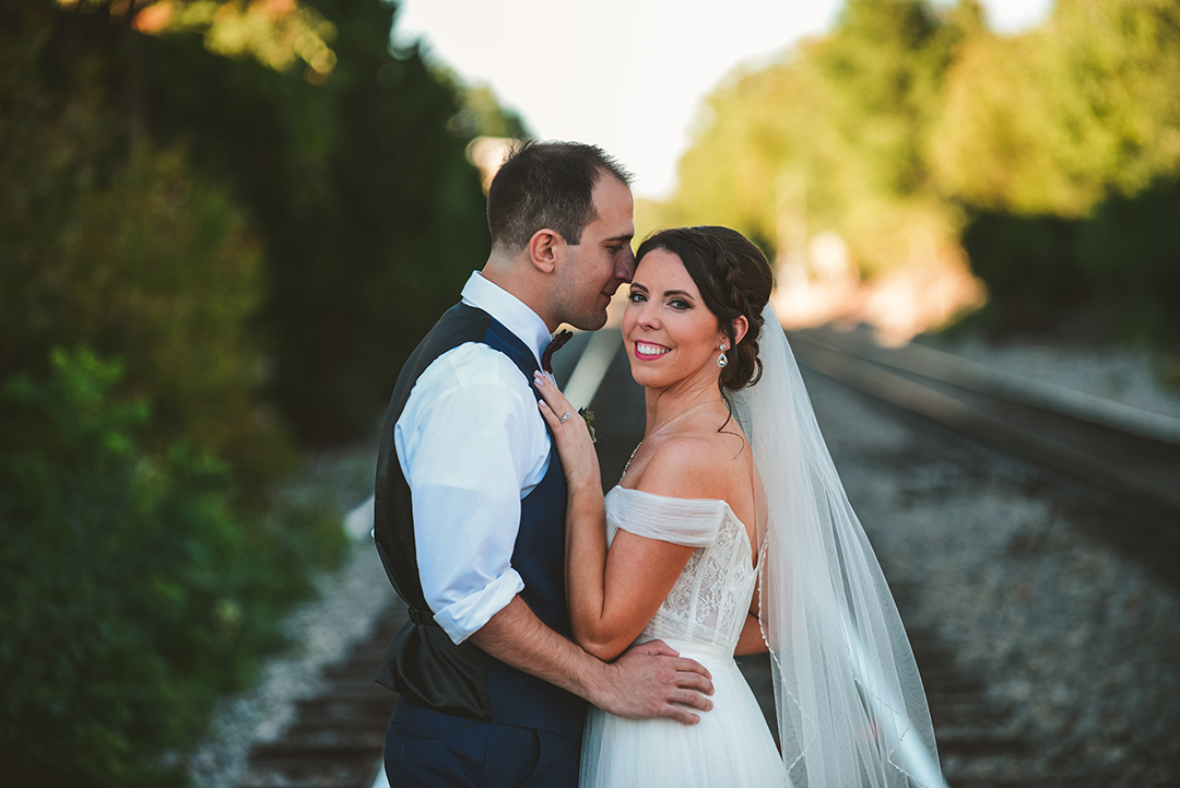 a groom pressing his head against his brides on a train track during the evening in Lockport IL