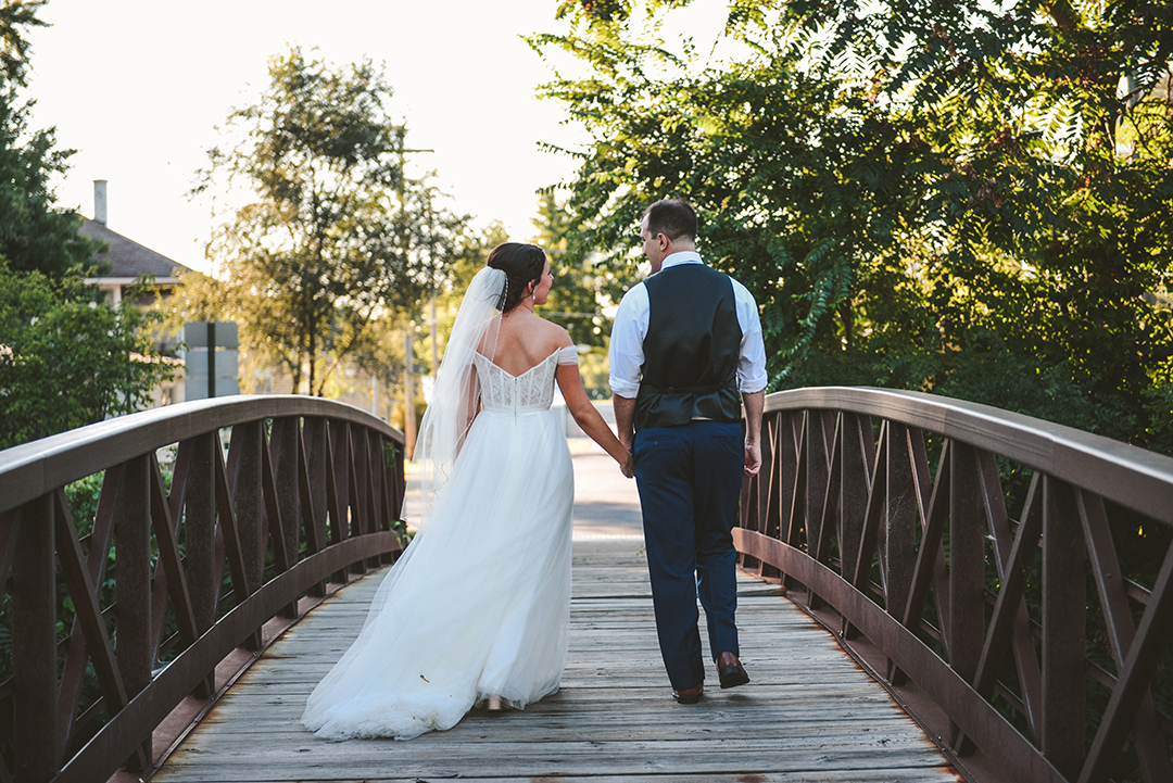 a bride and groom holding hands as they walk away on a old bridge in Lockport
