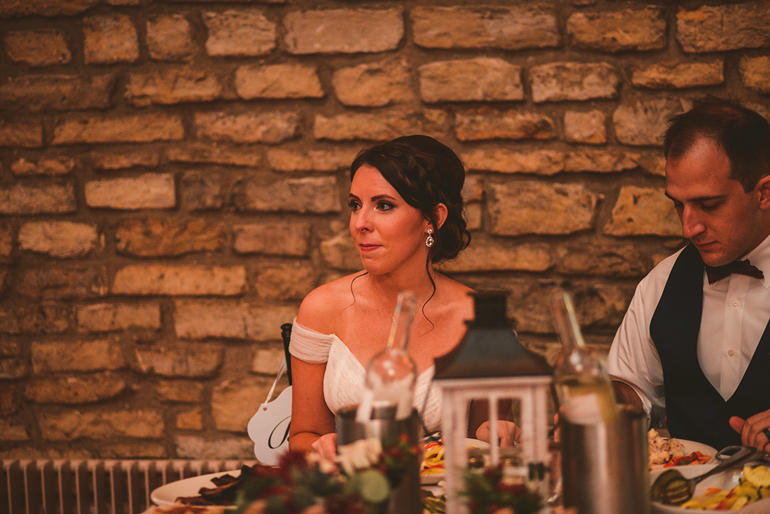 the bride smiling as her best friend gives a speech at her wedding reception