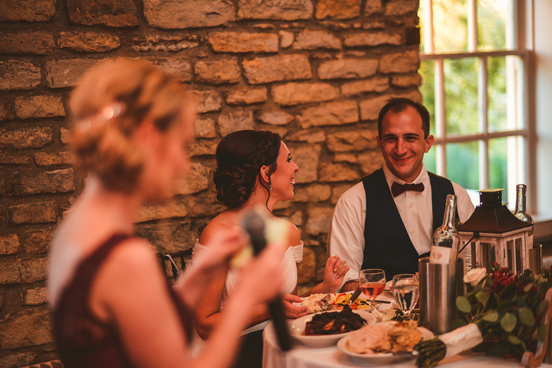 a bride and groom laughing as the maid of honor gives a speech at their wedding reception in Lockport