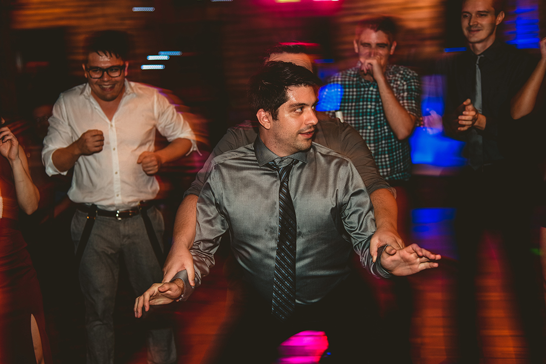 two guys dancing at a wedding reception as everyone laughs