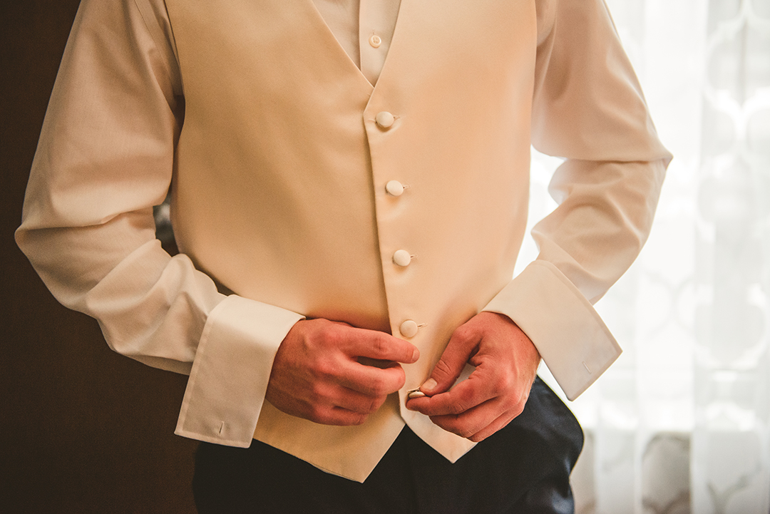 the groom buttoning his vest as he gets ready for his wedding at St Thomas Apostle Church in Naperville