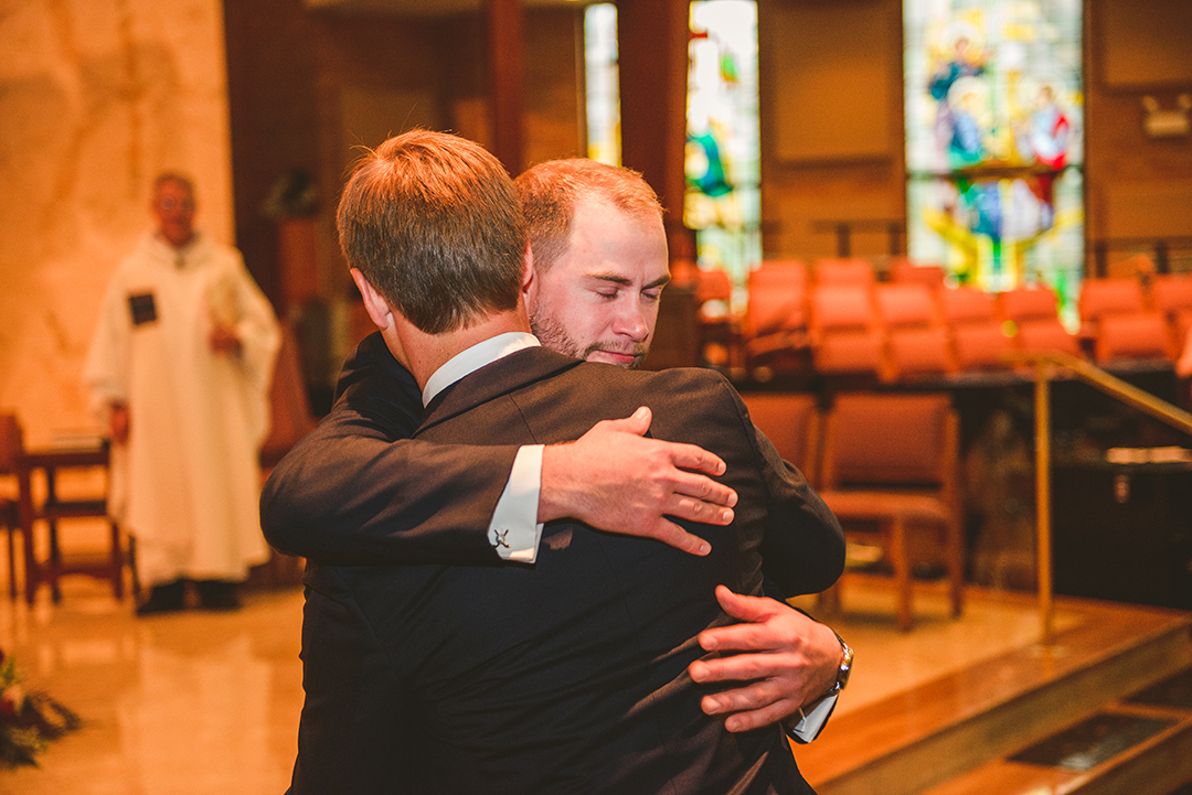 the groom hugging the best man right before his bride walks down the aisle at St Thomas Apostle Church in Naperville