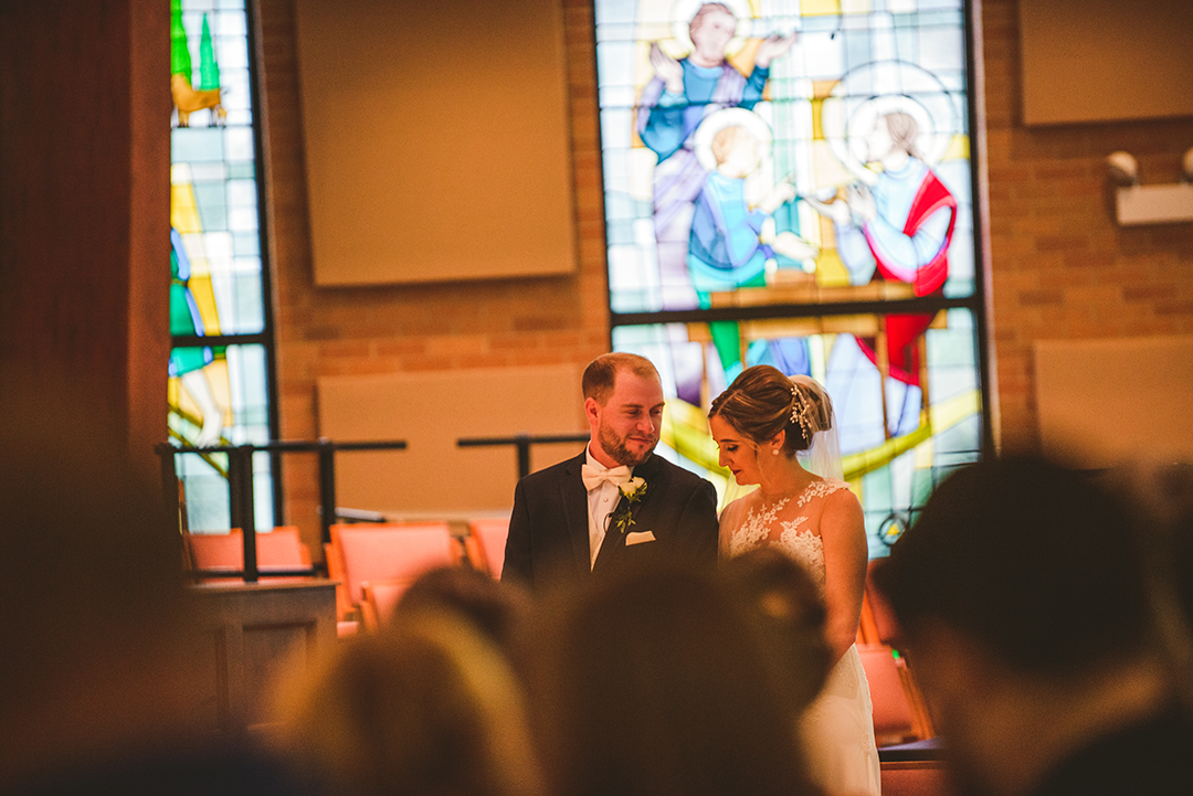 the groom smiling at his bride during the ceremony as all their wedding guests watch at St Thomas Apostle Church in Naperville