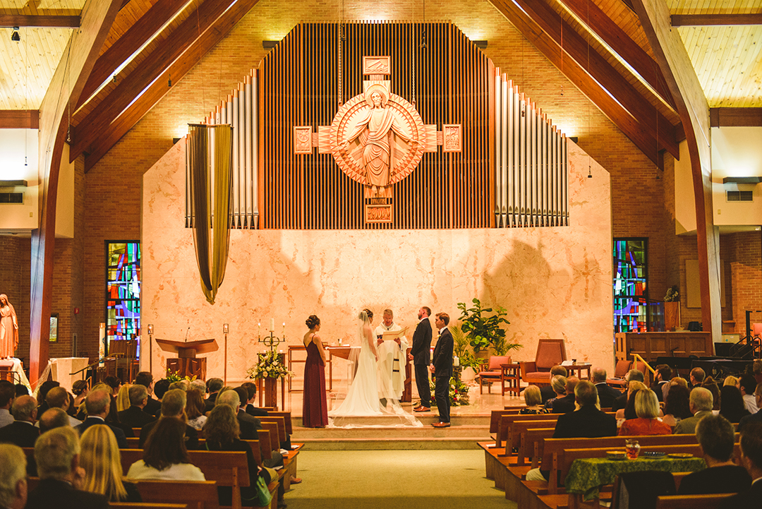 a bride and groom standing at the alter at St Thomas Apostle Church in Naperville as all of their friends and family watch