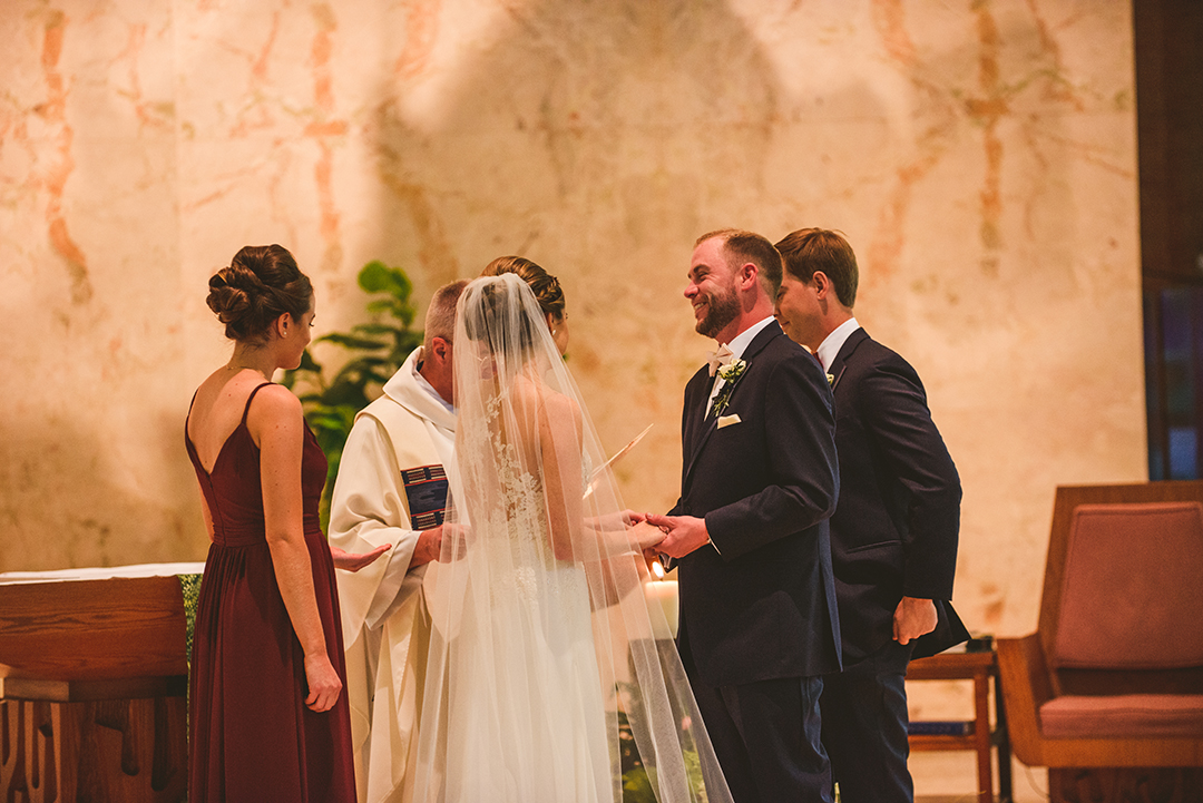 the groom laughing as he holds onto his brides hands while getting married