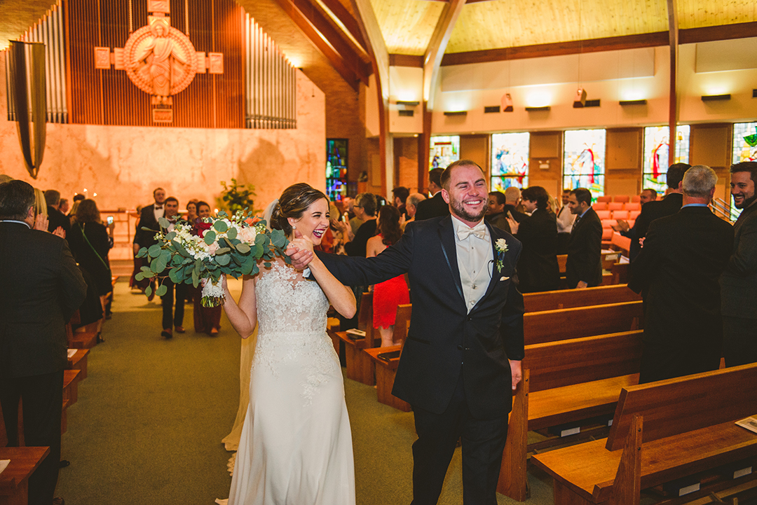 the bride and groom laughing as they walk down the aisle after being married at St Thomas Apostle Church in Naperville