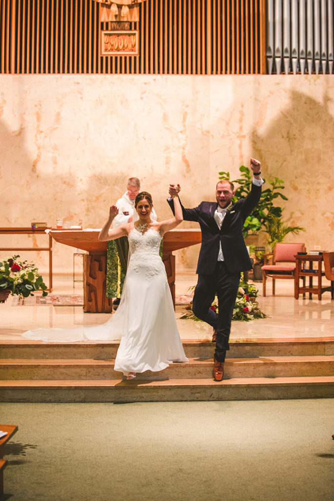 the bride and groom throwing up their arms as they celebrate getting married at St Thomas Apostle Church in Naperville