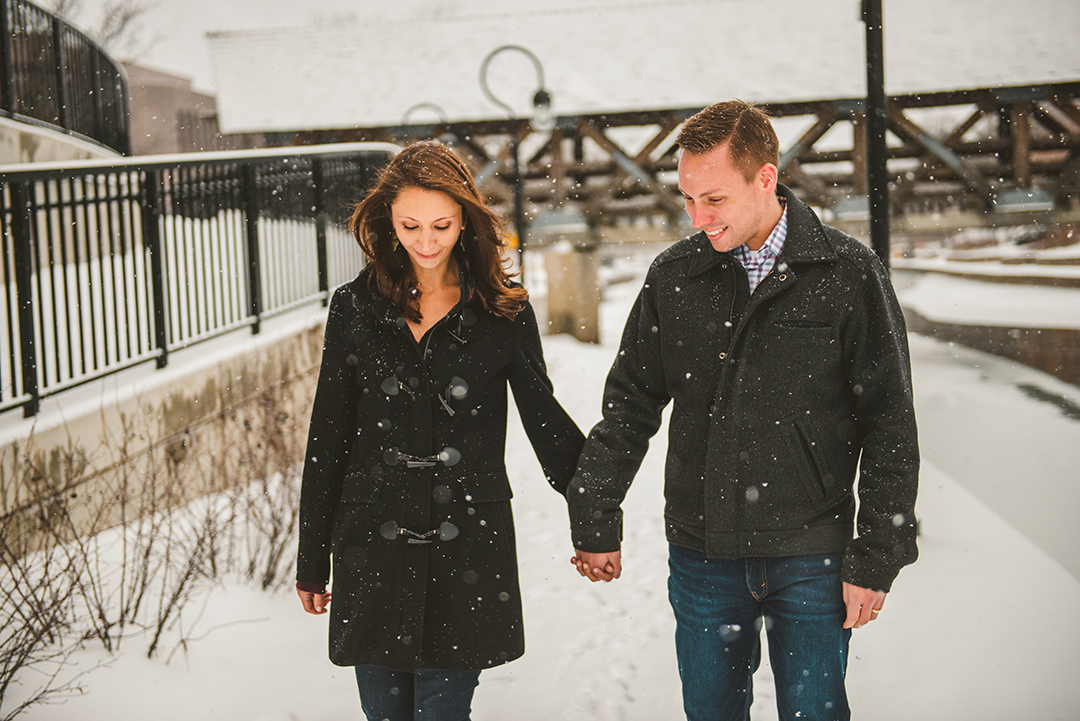 a couple holding hands as they walk in the snow on the Naperville riverwalk