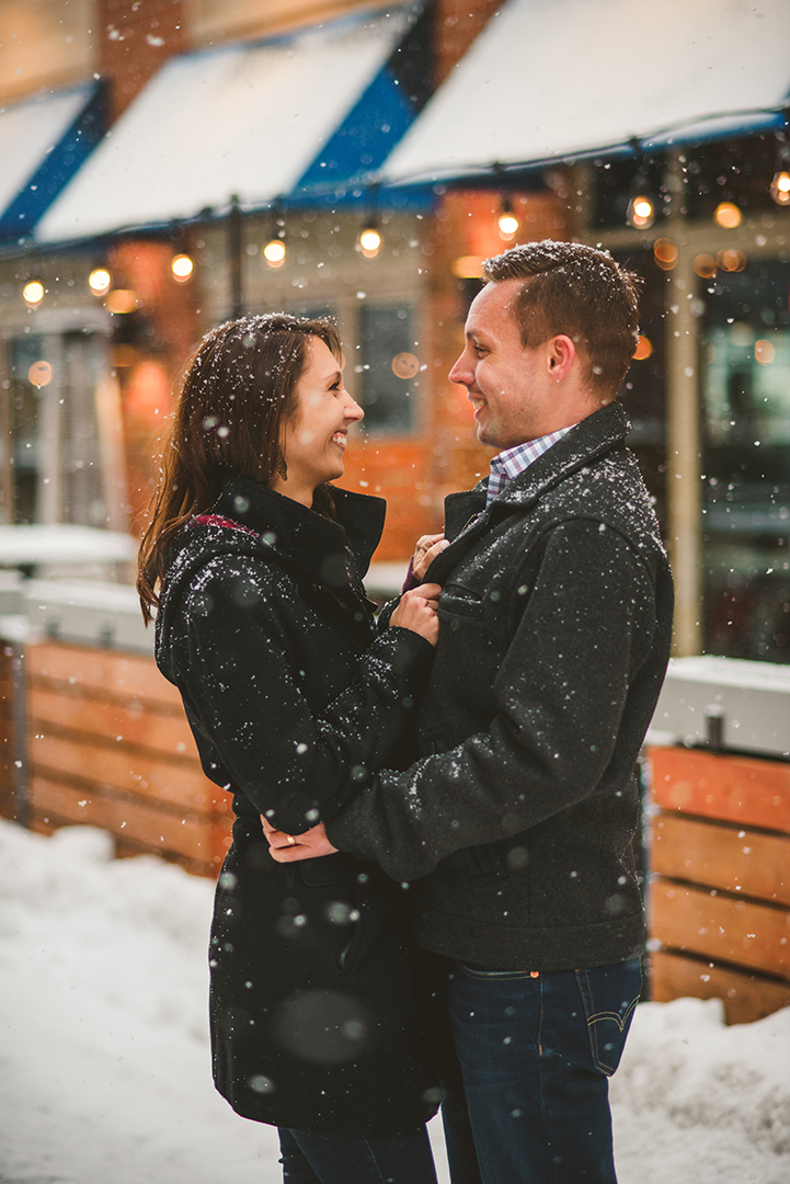 a bride holding onto her groom as they stand in the snow as they look into each others eyes in the snow