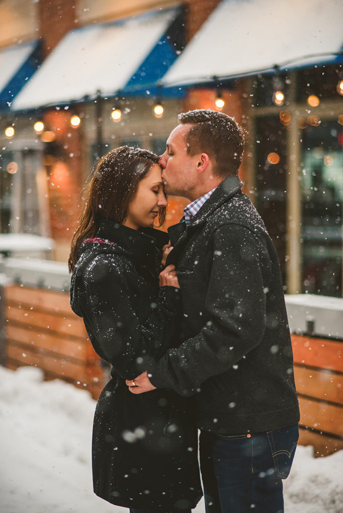a groom kissing his brides head as they stand in the snow on the Naperville Riverwalk