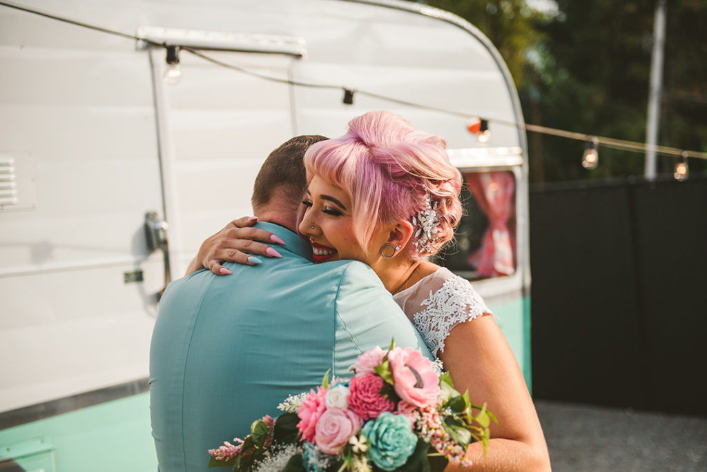 A bride and groom hugging in front of an old trailer after their first look