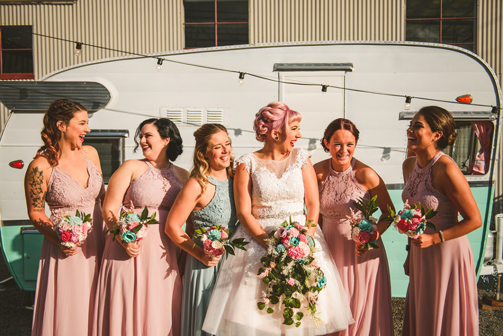 the bridesmaids laughing as they stand in front of a rustic camper at the Warehouse 109 in Plainefield
