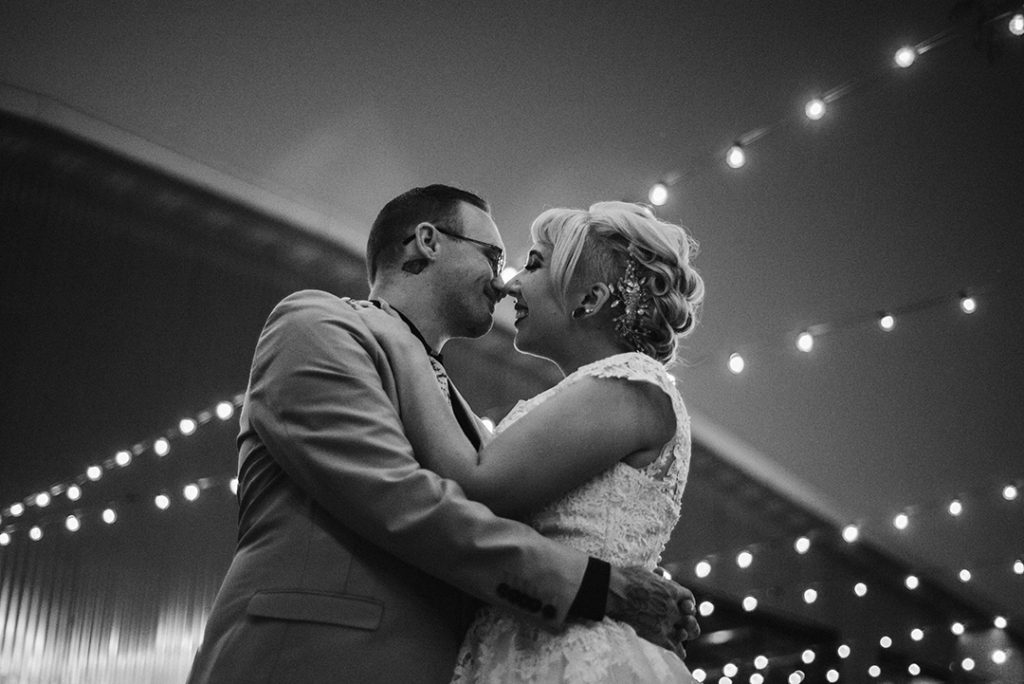 a bride and groom standing under string lights in the evening at the Warehouse 109 as they smile at each other