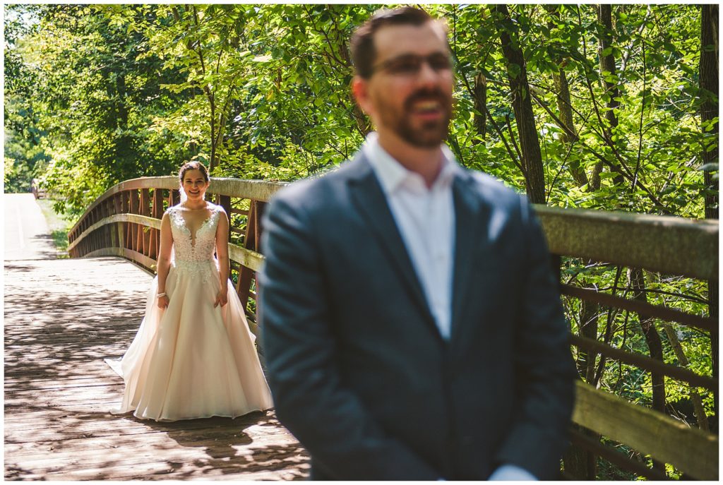 bride smiling behind a grooms back right before their first look right before a lake wedding