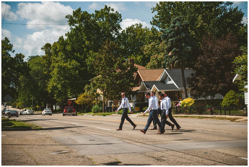 the groomsmen walking across the street to their car before their summer lake wedding at Lake Bloomington