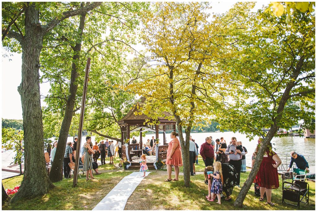 wedding guests socializing before a summer lake wedding at Lake Bloomington by a handmade wooden gazebo