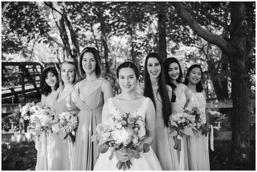 a bride standing with her stunning bridesmaids as everyone smiles at a lake wedding in the summer
