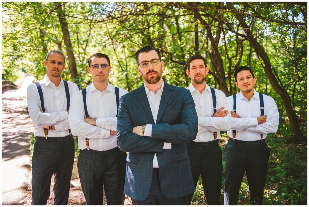 serious groomsmen standing together at a summer lake wedding