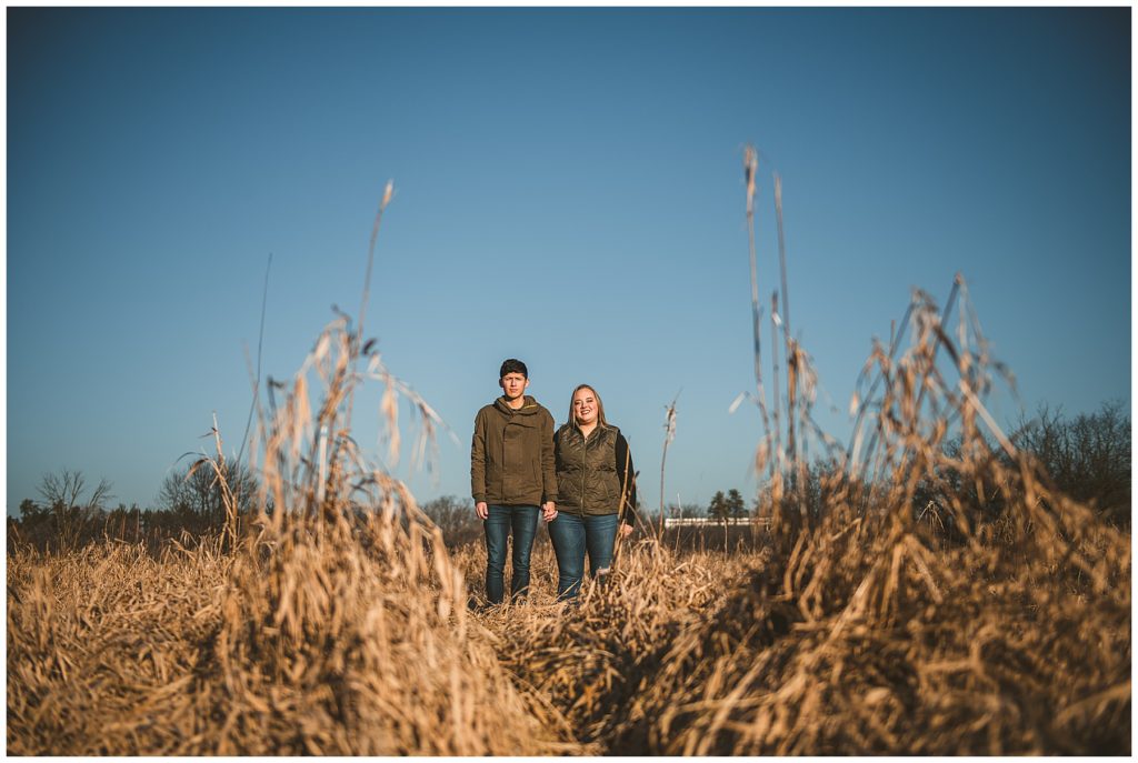 Rustic Engagement Photos of a bride and groom standing far away in a field with a clear blue sky