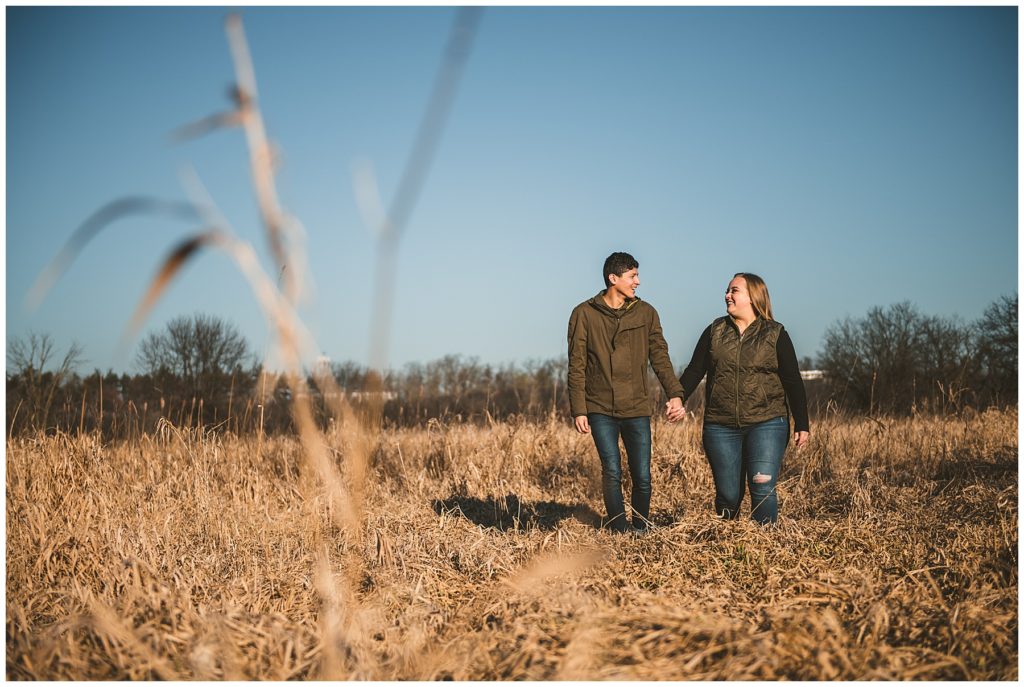 Rustic Engagement Photos of a man and a woman walking in a field in the early morning of winter with a clear blue sky