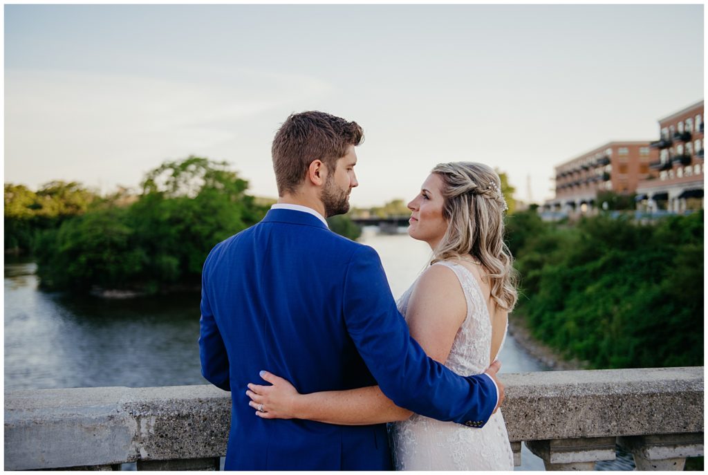 the bride and groom standing on a bridge over the fox river in downtown Aurora