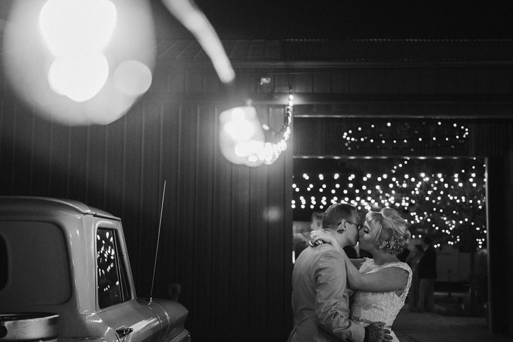 a grainy black and white photo of a bride and groom kissing by some Edison bulbs