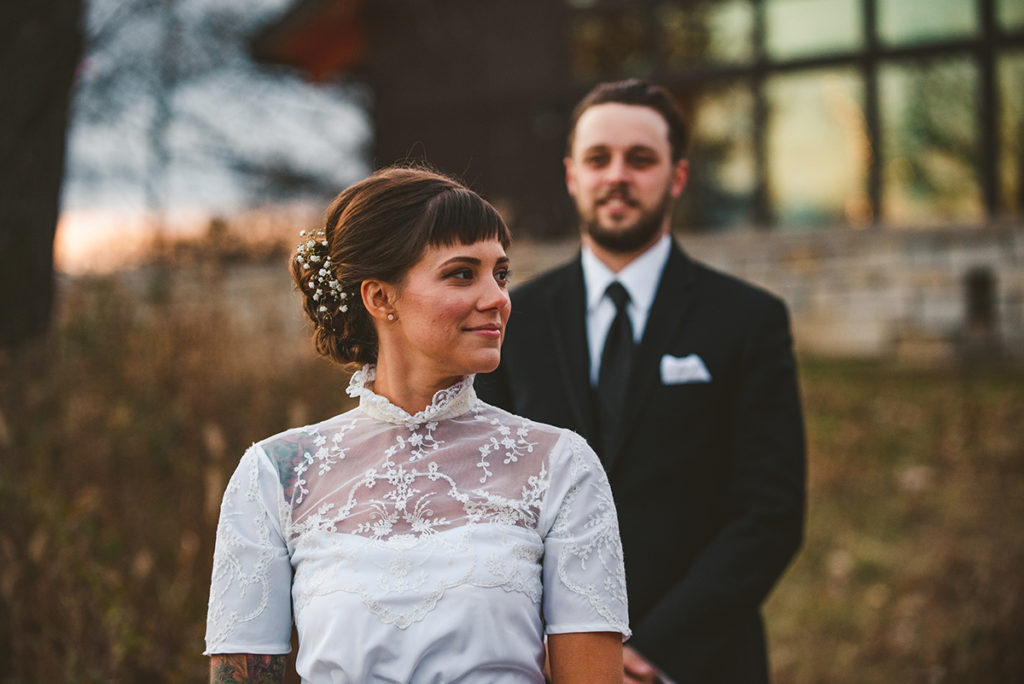a bride wearing a vintage dress as she stands with her groom at sunset