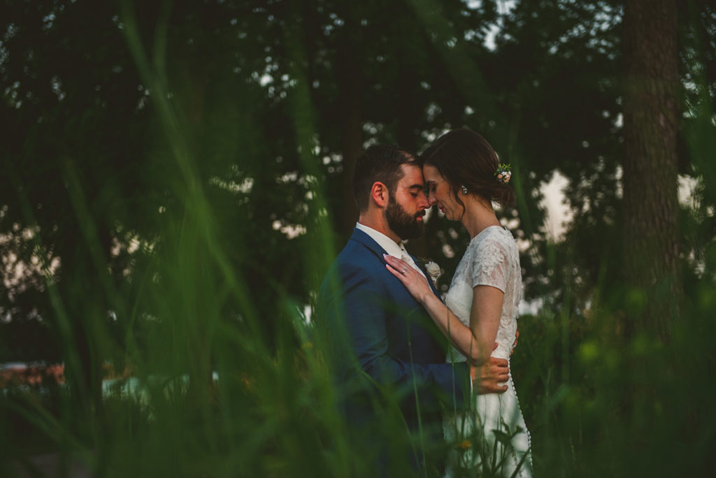 a bride and groom hugging close together as the sun sets in the evening of their summer wedding