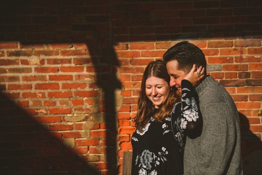 a man and a woman hugging and laughing in beautiful golden light with red brick in the background