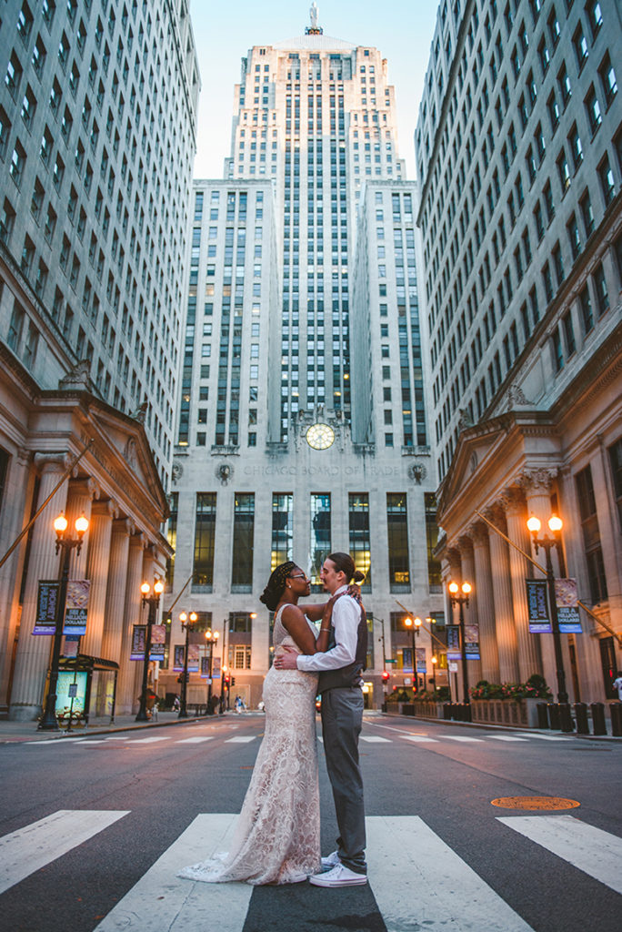 a bride and groom getting close together in the middle of the street as the sun sets on the building around them