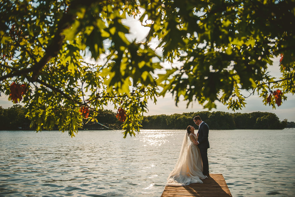 a husband and wife getting close together as they laugh at sunset on an old wooden dock