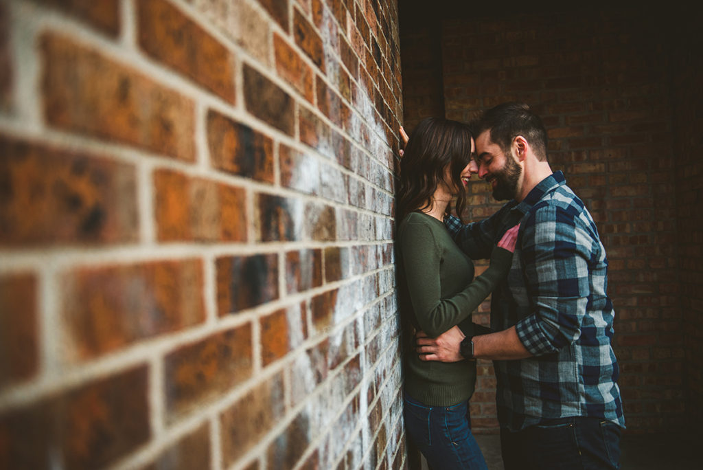 a man and a woman standing with their heads together against a old brick wall with artwork on it