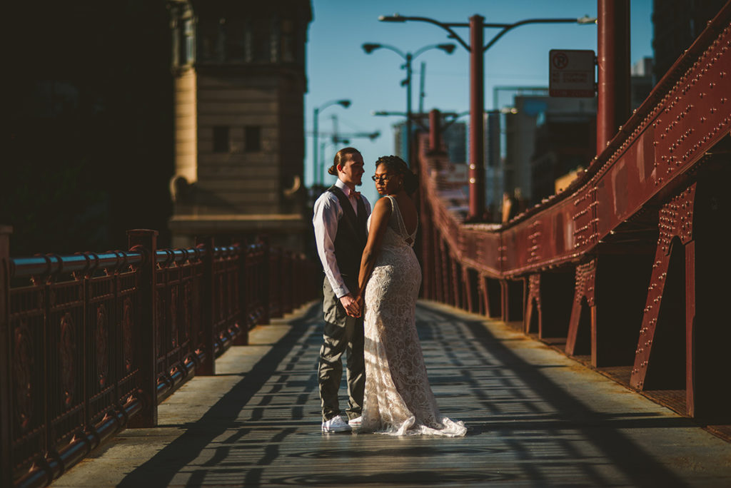 a bride in a vintage wedding dress stands on one of the old bridges of Chicago as the golden sun washes over them