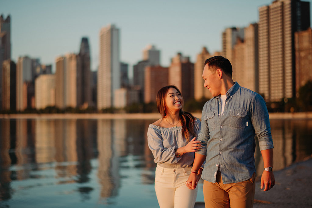 a husband and wife walking with their arms around each other at sunrise with the Chicago skyline in the background