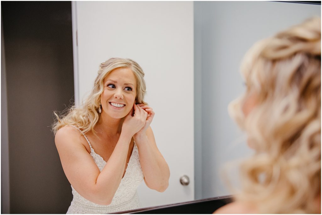 the bride putting on her ear rings in a well lit bathroom