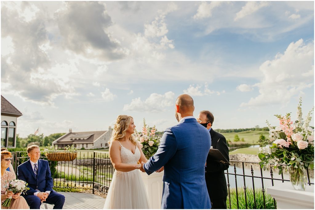 the bride and groom holding hands with a cloudy sky in the background on a summer evening